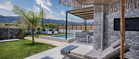 A modern outdoor patio with lounge chairs, a pool, and a stone wall backdrop.