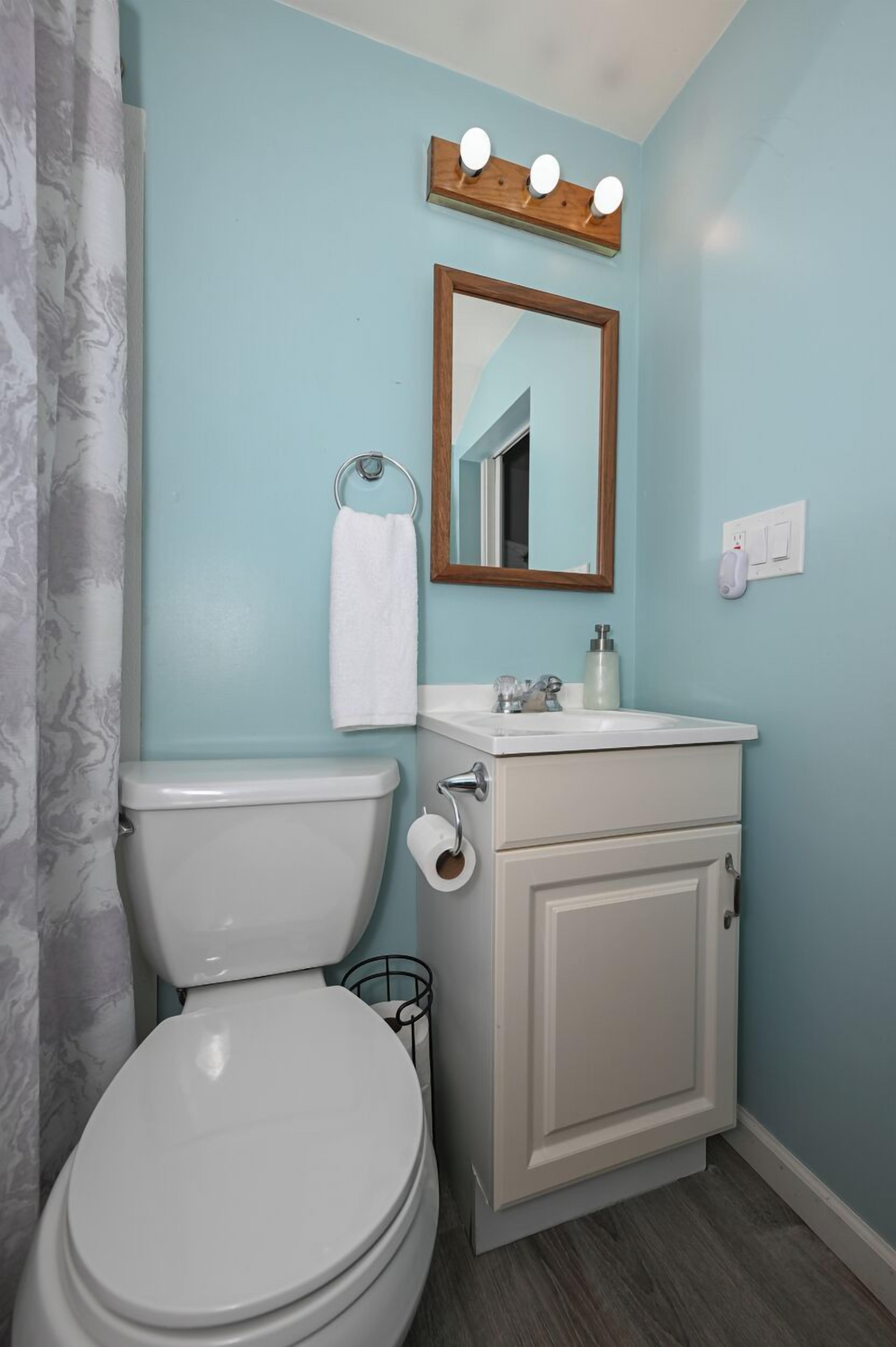 A bathroom with a toilet, sink, mirror, and towel rack.