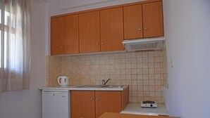 A compact kitchen with wooden cabinets, a small sink, a kettle, and a weighing scale. - Nikos Apartments A8 in Gialiskari (Ikaria)
