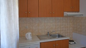 A kitchen with wooden cabinets, a stainless steel sink, a kettle, and a portable stove. - Nikos Apartments A8 in Gialiskari (Ikaria)