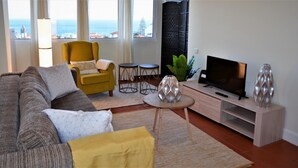 Sala de estar com sofá, poltrona, mesa de centro, televisão e vista para o mar.