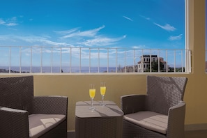Ein Balkon mit Korbmöbeln und zwei Gläsern Orangensaft, mit Blick auf die Küste.