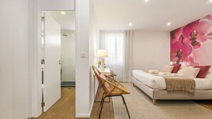 Een slaapkamer met een bed, een nachtkastje, een lamp, een stoel en een bloemig behang.