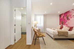 A bedroom with a bed, a bedside table, a lamp, a chair, and a wall with a floral mural.