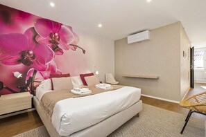 A modern bedroom with a large bed, a wall-mounted air conditioner, and a bright window.