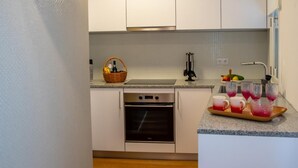 Een kleine keuken met witte kastjes, een inbouwoven en een klein aanrecht.