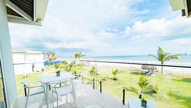 Un balcon avec vue sur la plage, une table, des chaises et une baignoire.