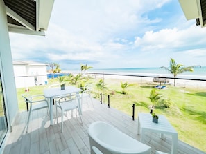Un balcon avec vue sur la plage, une table, des chaises et une baignoire.