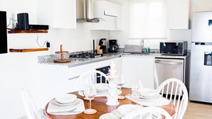 Une cuisine moderne avec des meubles blancs, une table à manger en bois et un luminaire suspendu en rotin.