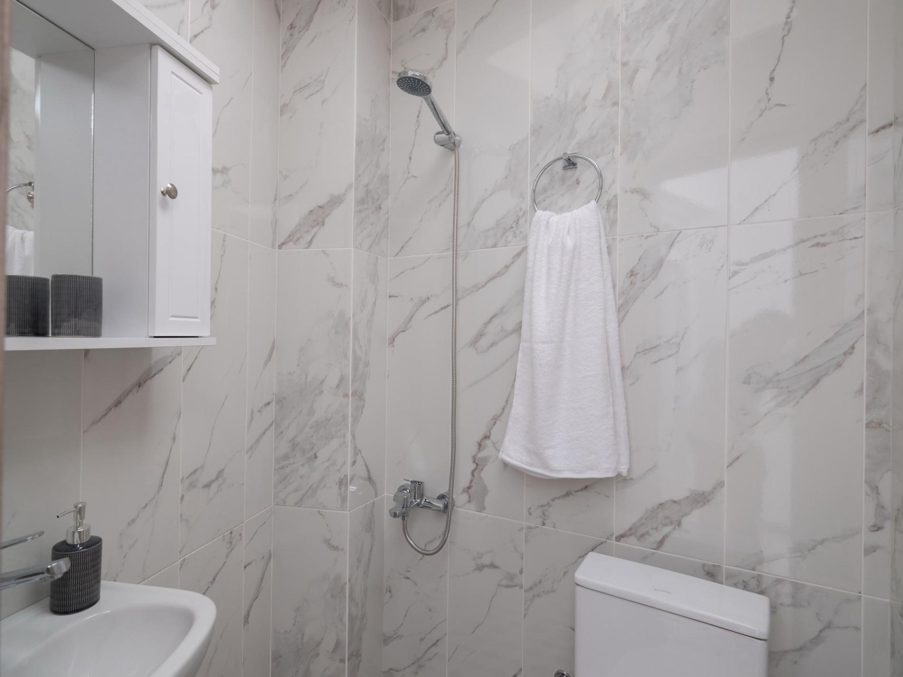 A bathroom with a marble wall, a white sink, a toilet, and a shower with a towel hanging on the wall.