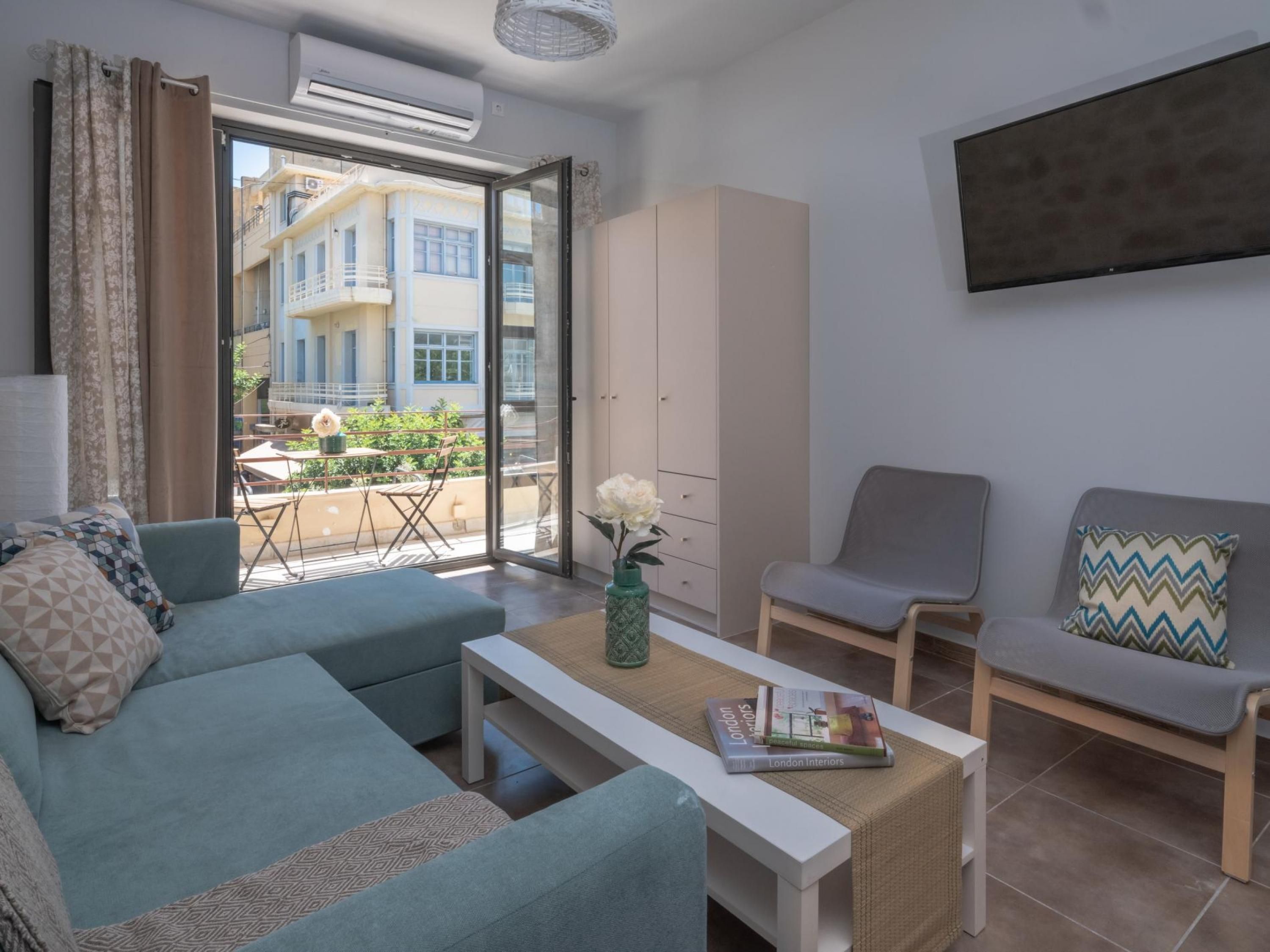 Un salon moderne avec un canapé, un fauteuil et une table basse. Une porte-fenêtre coulissante donne accès à un espace extérieur aménagé avec une table et des chaises. Un livre intitulé « Intérieurs londoniens » est posé sur la table basse.