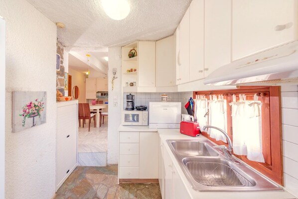 A compact kitchen with white cabinets, a built-in oven, a coffee maker, and a red suitcase. - The Kokkini Beach Retreat (Hersonissos)