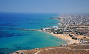 Vue aérienne d’une ville côtière avec une plage, un port de plaisance et un mélange de bâtiments résidentiels et commerciaux.