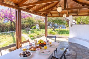 An outdoor dining area with a table set for breakfast, surrounded by stone flooring and wooden beams. - The Kokkini Beach Retreat (Hersonissos)