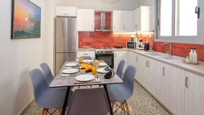 A modern kitchen with white cabinets, a stainless steel refrigerator, a dining table with chairs, and a large window. - The Museum View Suite (Heraklion)