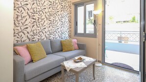 A living room with a grey sofa, patterned wallpaper, a small table with a placemat, and a view of the outside through a glass door. - The Museum View Suite (Heraklion)