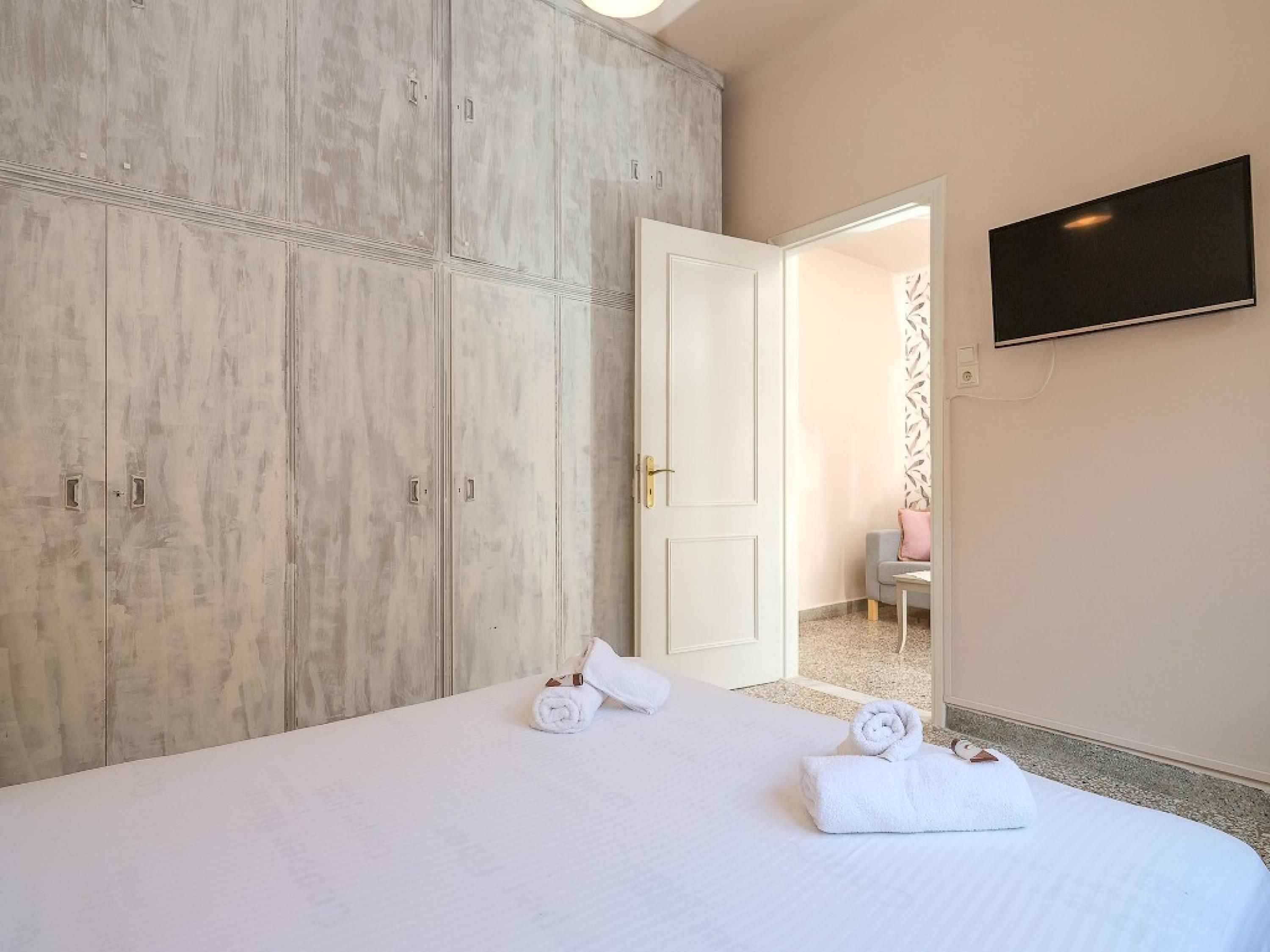 Habitación de hotel con un armario amplio, una cama con ropa blanca y un televisor de pantalla plana montado en la pared.