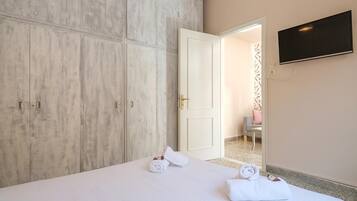 Habitación de hotel con un armario amplio, una cama con ropa blanca y un televisor de pantalla plana montado en la pared.
