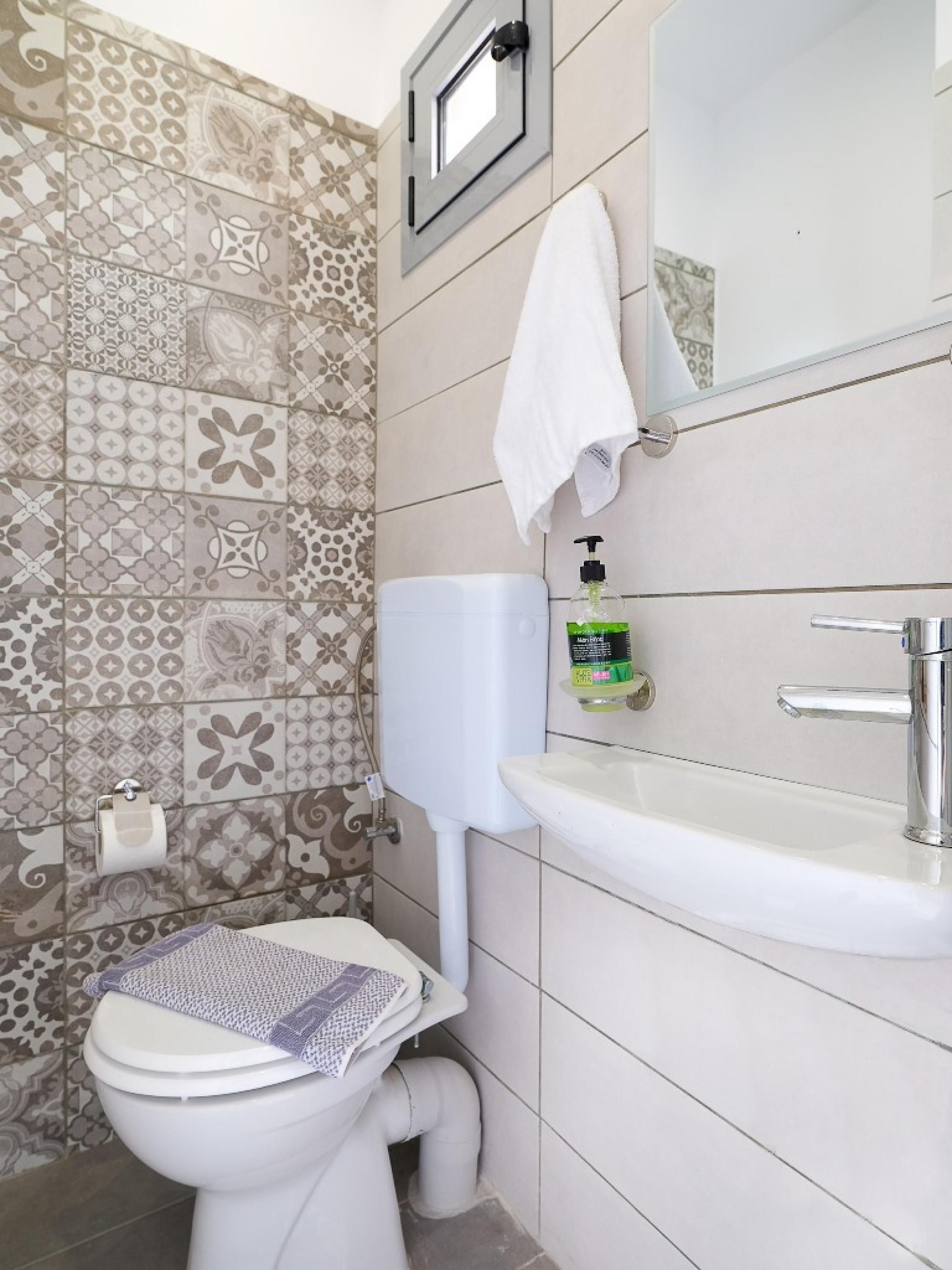 Ein Badezimmer mit gemusterten Fliesen, einer Toilette, einem Waschbecken, einem Spiegel und einem Handtuchhalter.