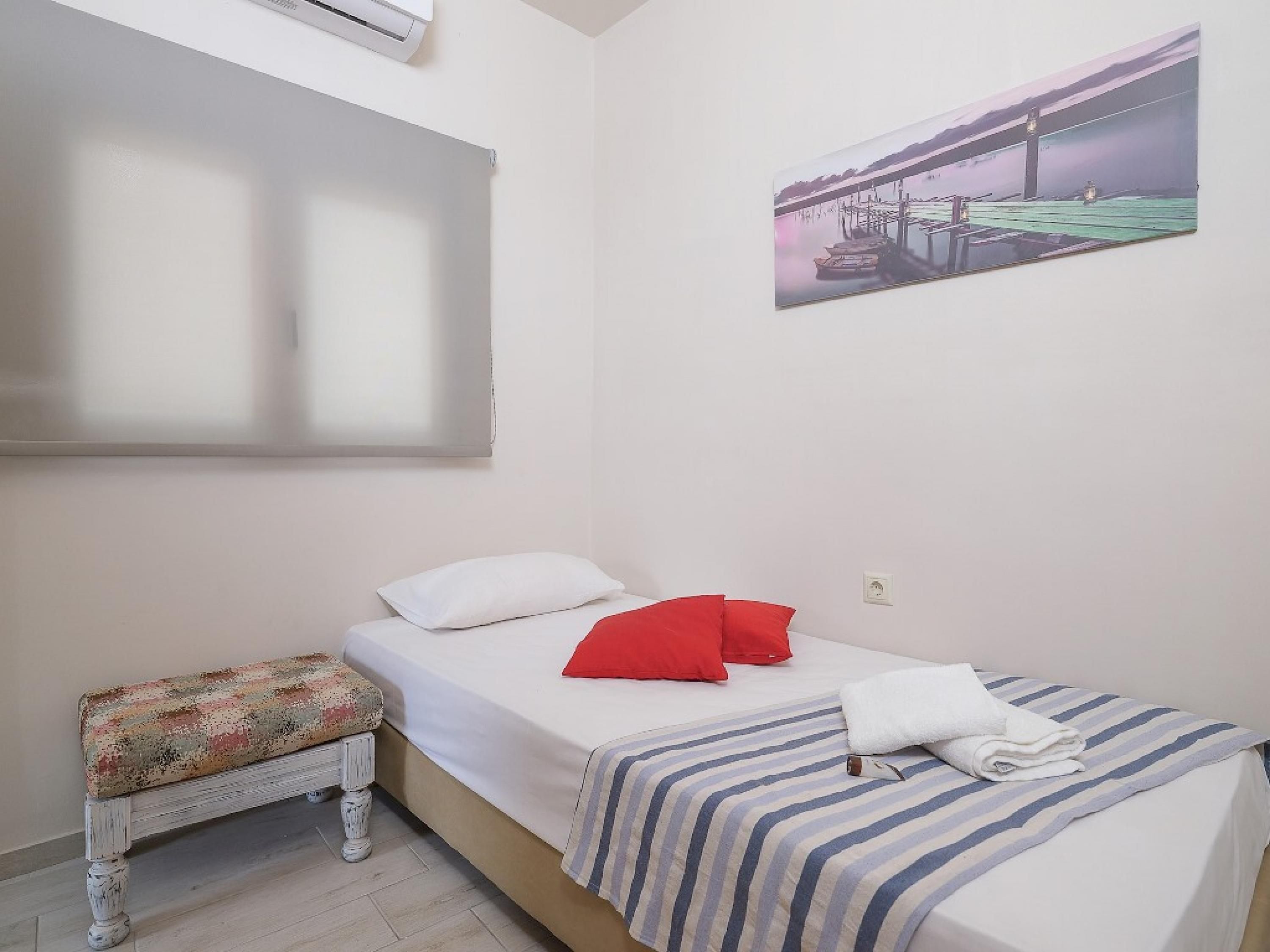 Un dormitorio con cama, un banco, un cuadro y un equipo de aire acondicionado.