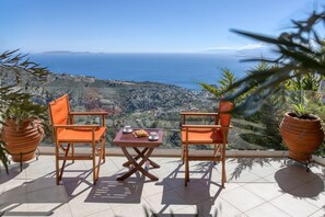 A terrace with two wooden chairs and a small table, overlooking a coastal landscape with a clear view of the sea and distant hills. - Vista Mare Villa by Estia (Malevizi)