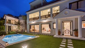 Et moderne hus med to etager, swimmingpool, udendørs siddepladser og en godt oplyst indgang.