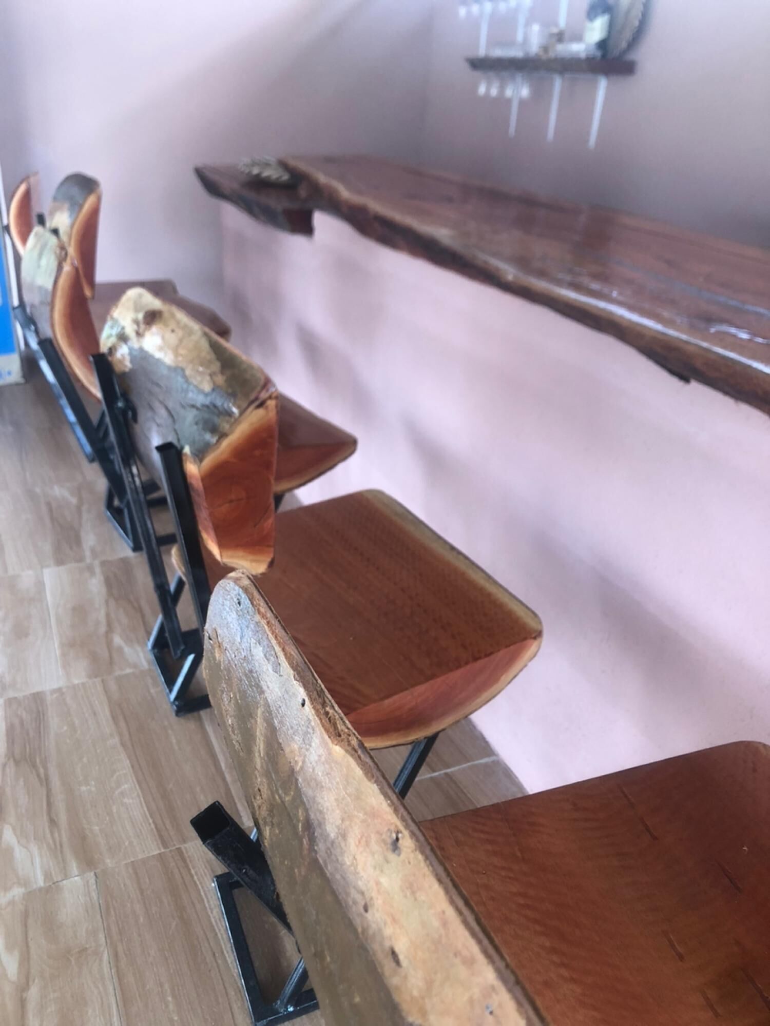 Filera de taules i cadires de fusta en una habitació amb terra de rajola i paret rosa.