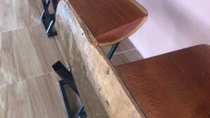 A row of wooden desks and chairs in a room with a tiled floor and a pink wall. - 1 bed Apartment in Mount Pleasant Heights - 2014 (Harare)