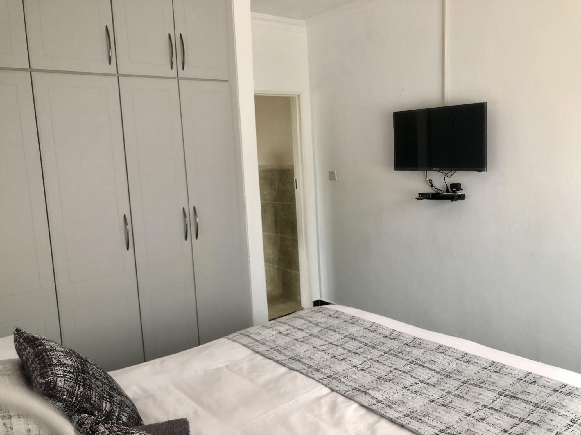 Un dormitorio con una cama, un armario gris y un televisor montado en la pared.