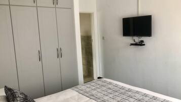 Un dormitorio con una cama, un armario gris y un televisor montado en la pared.