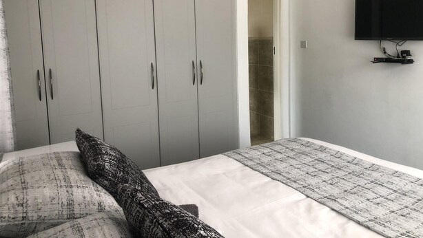 A bedroom with a bed, grey wardrobe, and a mounted TV. - 1 bed Apartment in Mount Pleasant Heights - 2014 (Harare)
