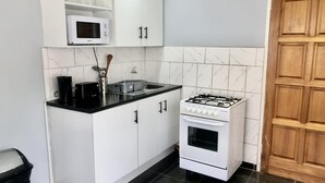 A compact kitchen with white cabinets, a white gas stove, a microwave, and a black coffee maker. - 1 bed Apartment in Mount Pleasant Heights - 2014 (Harare)