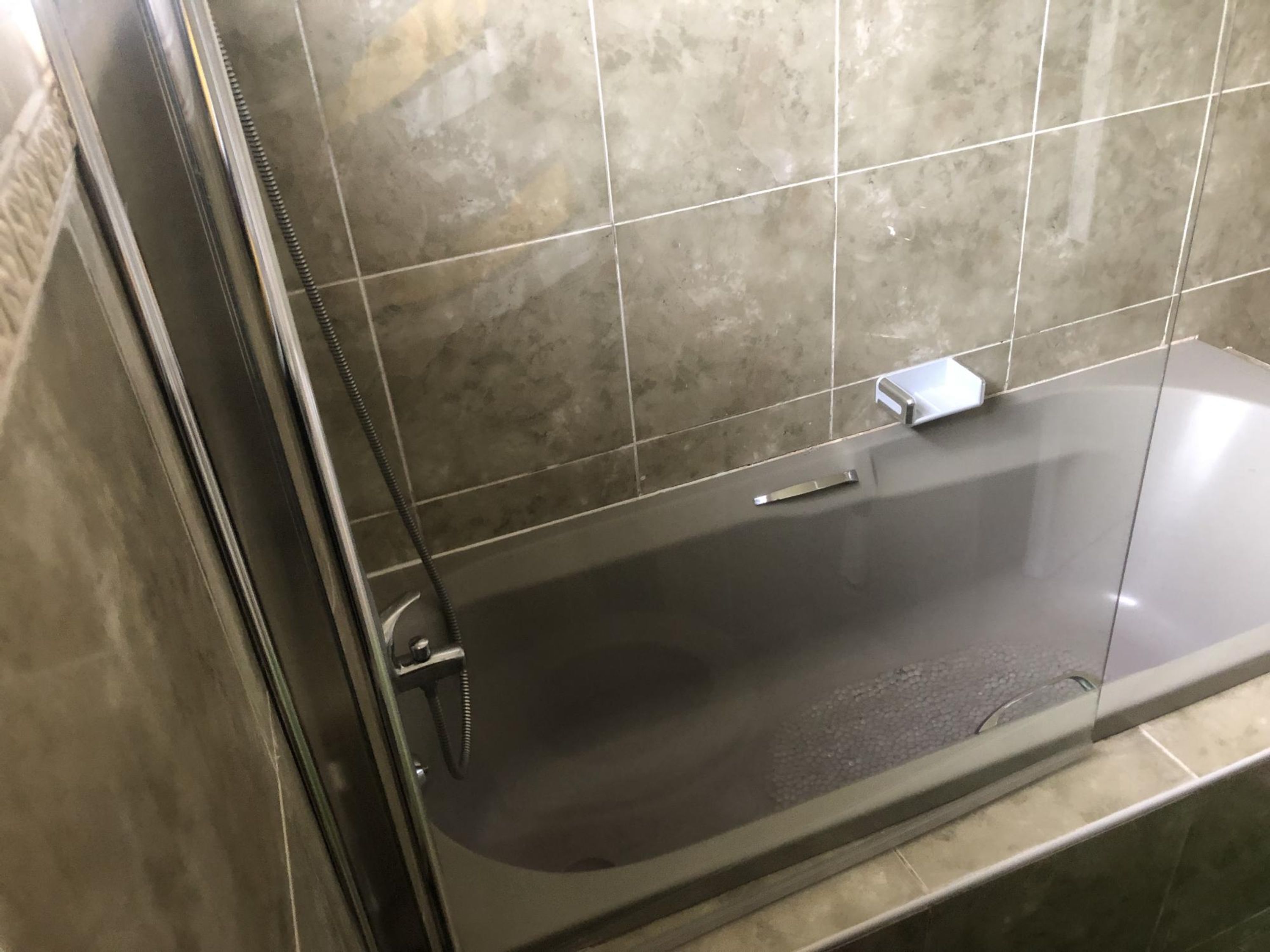A bathroom with a glass-enclosed bathtub, a handheld showerhead, and a small, rectangular mirror.