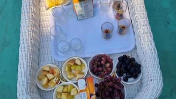 A wicker tray with fruits, a juice box, and glasses on a turquoise surface.