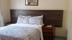 A bedroom with a bed, two nightstands, a wooden headboard, a mirror, and a patterned bedspread. - Neat and Cosy Cottage With Pool - 2103 (Harare)