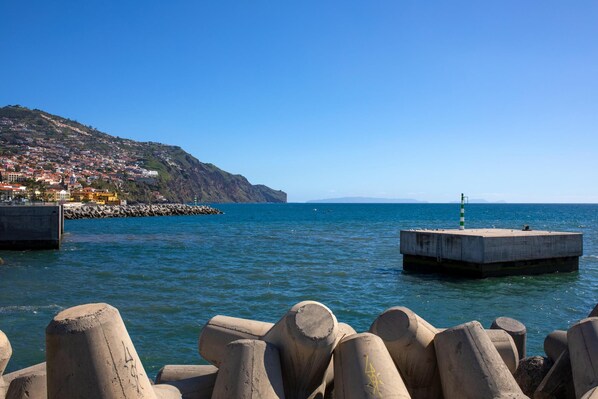 A coastal scene with a pier, a lighthouse, and a hillside town.