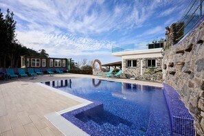 Relax by the pool surrounded by a deck and a stone wall with a glass railing.