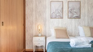 A bedroom with a wooden wardrobe, a bedside table with a lamp, a bed with white bedding and a teal blanket, and two framed wall art pieces. - Porto Moniz City Centre by Homie (Porto Moniz)