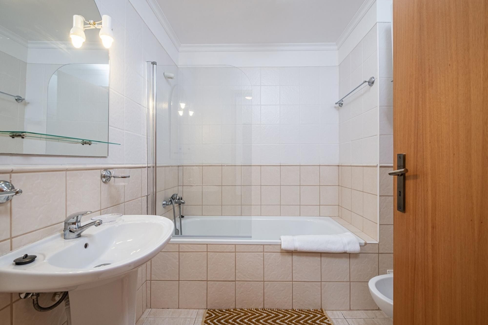 A bathroom with a bathtub, two sinks, a glass shower enclosure, and a wooden door.