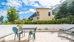 An outdoor patio with a table and chairs, a white wall, and a building in the background. - Porto Moniz City Centre by Homie (Porto Moniz)