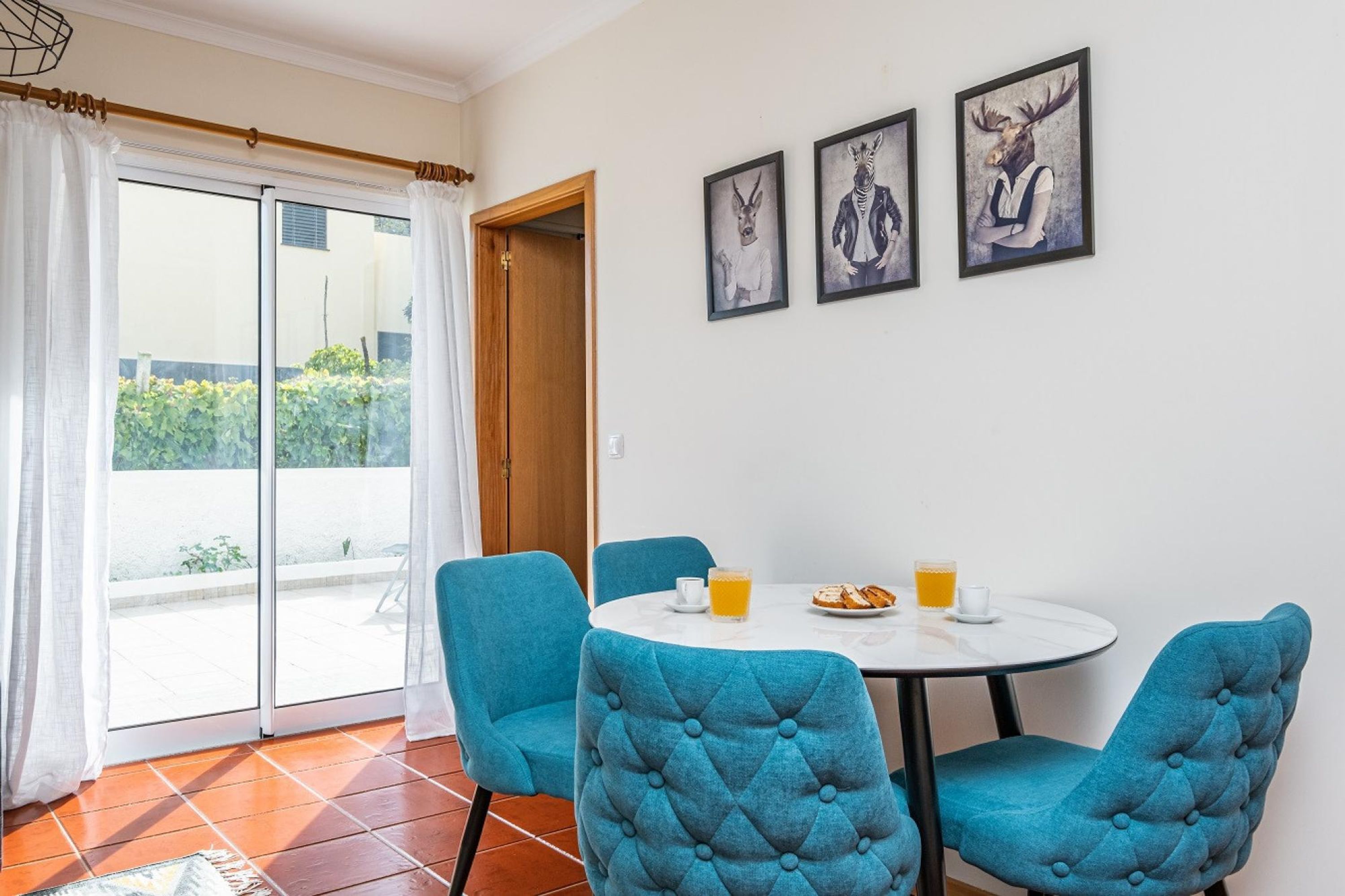 Un coin repas avec une table ronde, quatre chaises bleues à revêtement rembourré et trois œuvres d’art encadrées accrochées au mur.