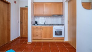 A compact kitchen with wooden cabinets, a built-in oven, and a tiled backsplash. - Porto Moniz City Centre by Homie (Porto Moniz)