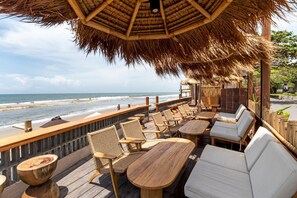 Relax in a serene ocean-view seating area with wicker chairs and tables under a thatched roof.