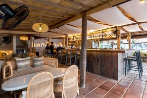 Relax in a rustic outdoor seating area with wicker tables and chairs, surrounded by a thatched roof and a bar counter.