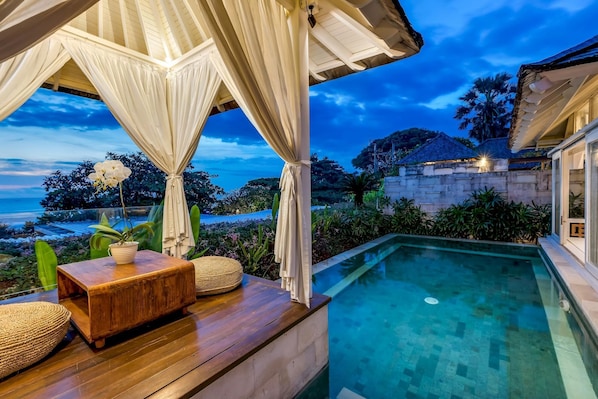 Relax by the pool surrounded by lush greenery and a distant sea view.