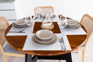 A dining table for four, set with a decorative sailboat centerpiece and wicker chairs with cushions.