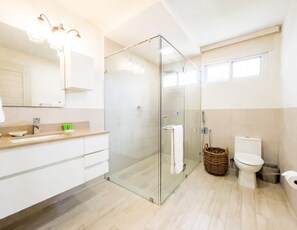 A modern bathroom with a glass-enclosed shower, a toilet, and a vanity with a mirror and countertop. - Olas del mar 1B in Chame (Punta Chame)