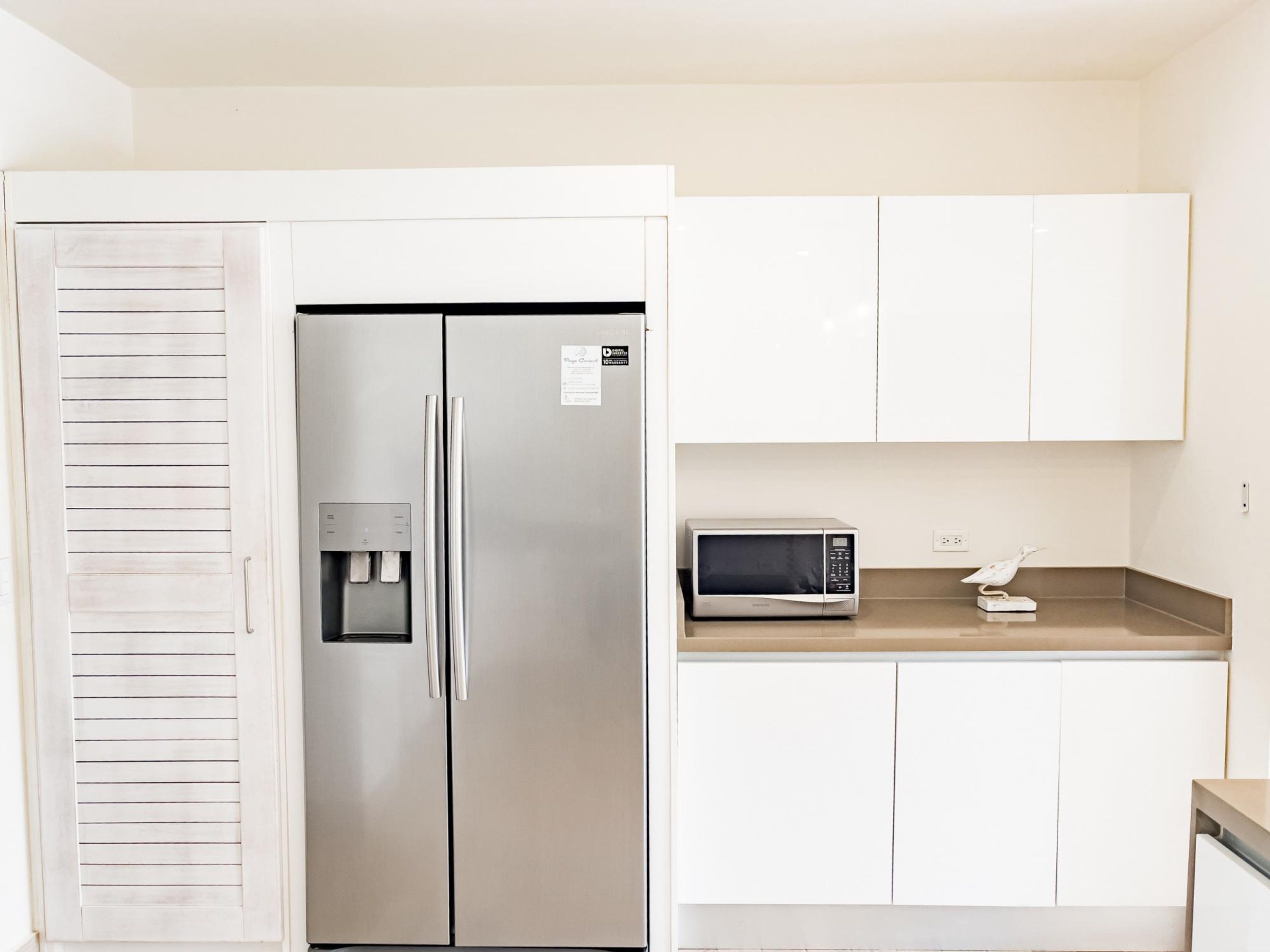 Una cocina con refrigerador de acero inoxidable, dispensador de agua, microondas y armarios blancos.