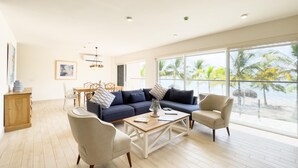 Un salon spacieux avec une grande fenêtre, un canapé bleu, un fauteuil beige et une table basse en bois.