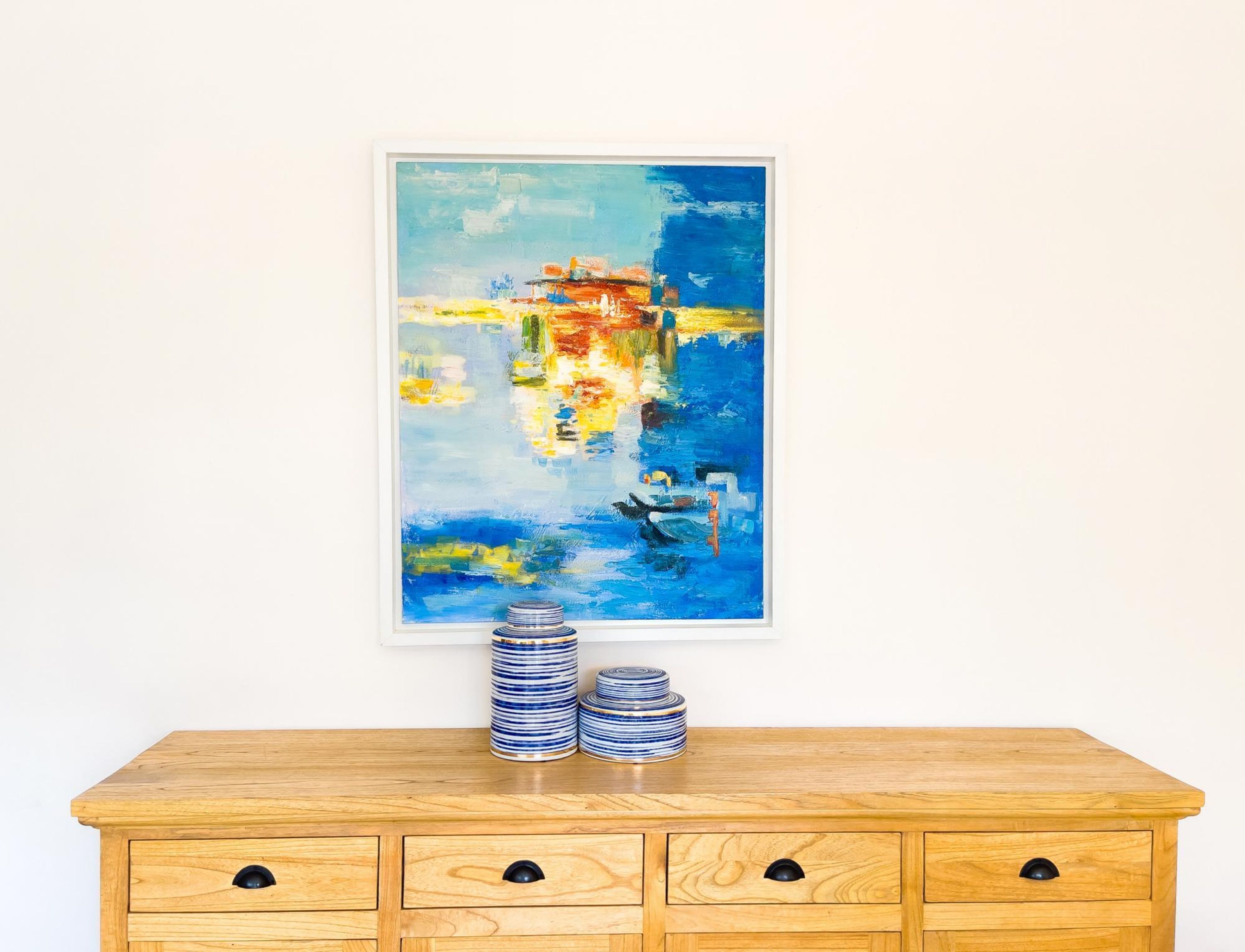 A wooden dresser with multiple drawers and a framed abstract painting above it.